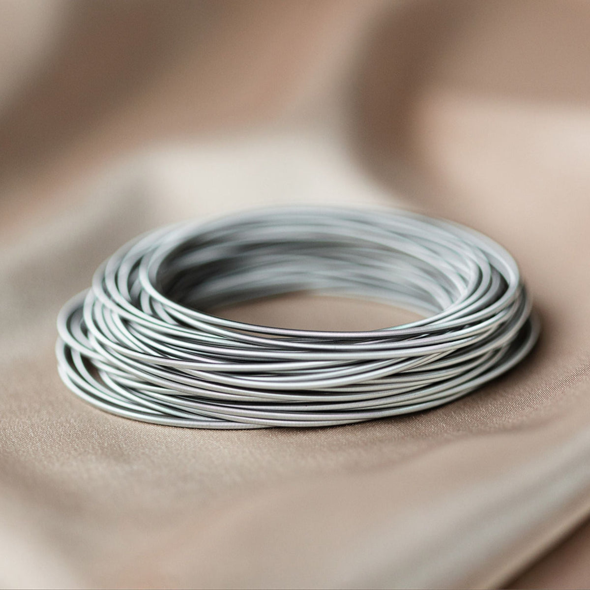 Thin silver-tone bangles stacked in a circular arrangement on soft fabric