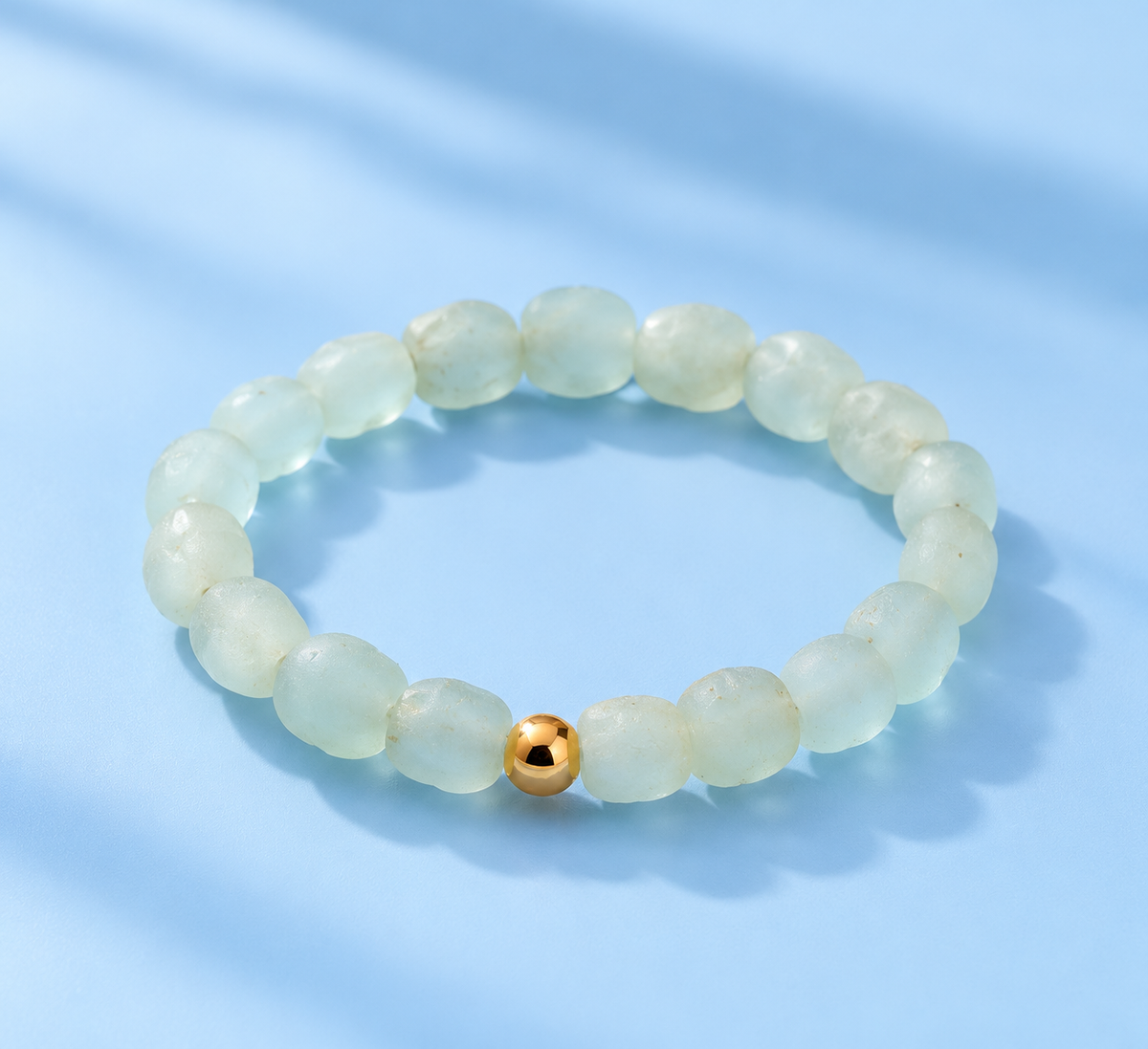 Sora bracelet featuring frosted blue-green sea glass beads and a single gold-filled accent on a pale-blue background — The Riann Ashlyn Collection.