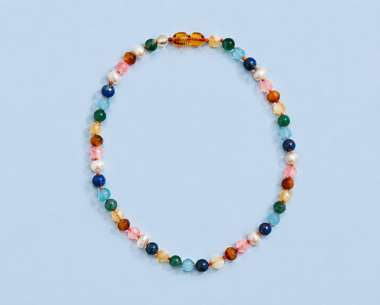 Sunday Necklace with multicolored natural gemstones, Baltic amber, and freshwater pearls arranged on a light blue background.