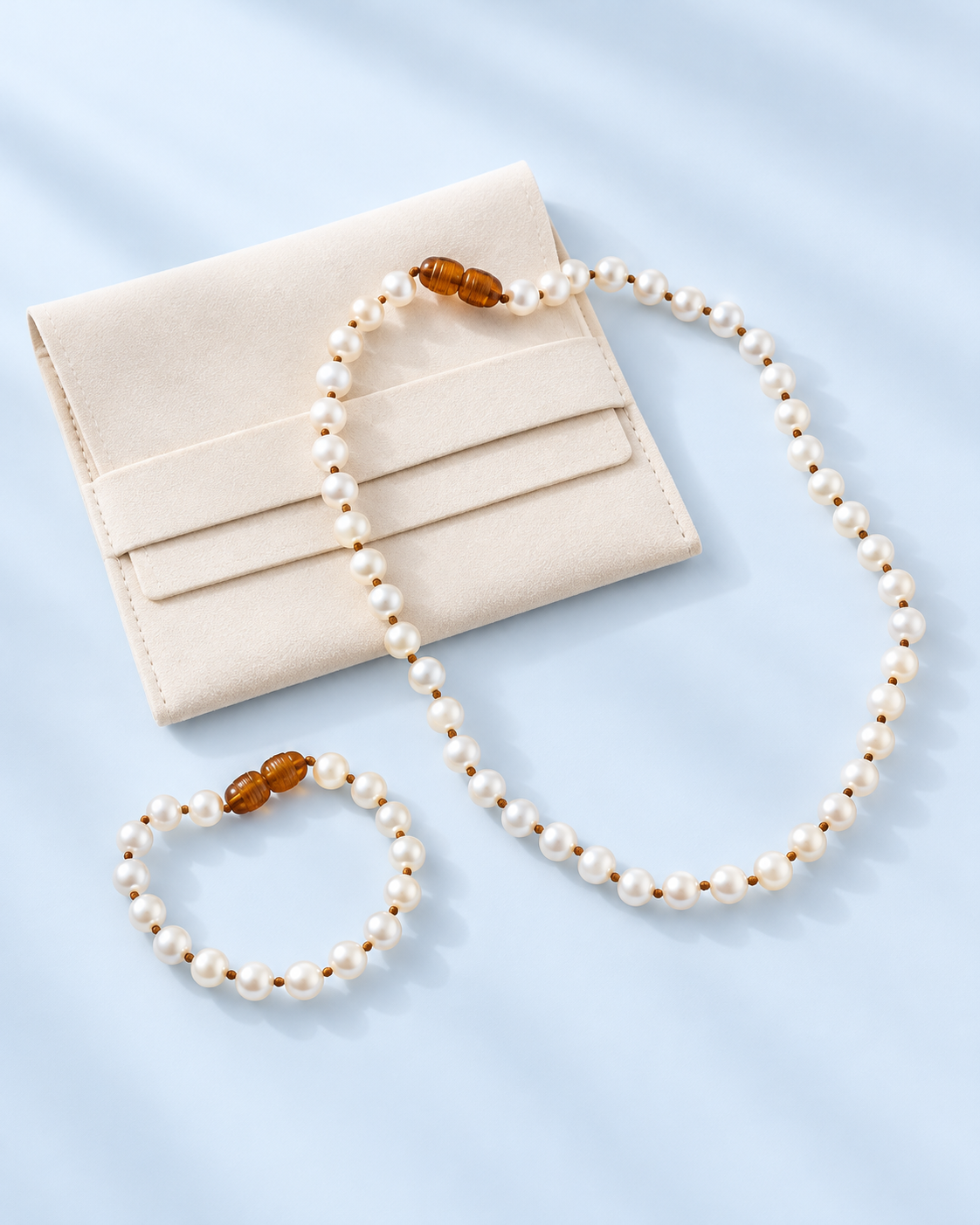 Tinsley pearl necklace and matching bracelet with amber-toned bead details arranged on a pale blue background, The Riann Ashlyn Collection.