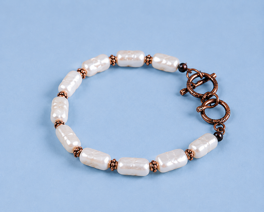 White rectangular pearl bracelet with copper-tone spacer beads and toggle clasp on a light blue background
