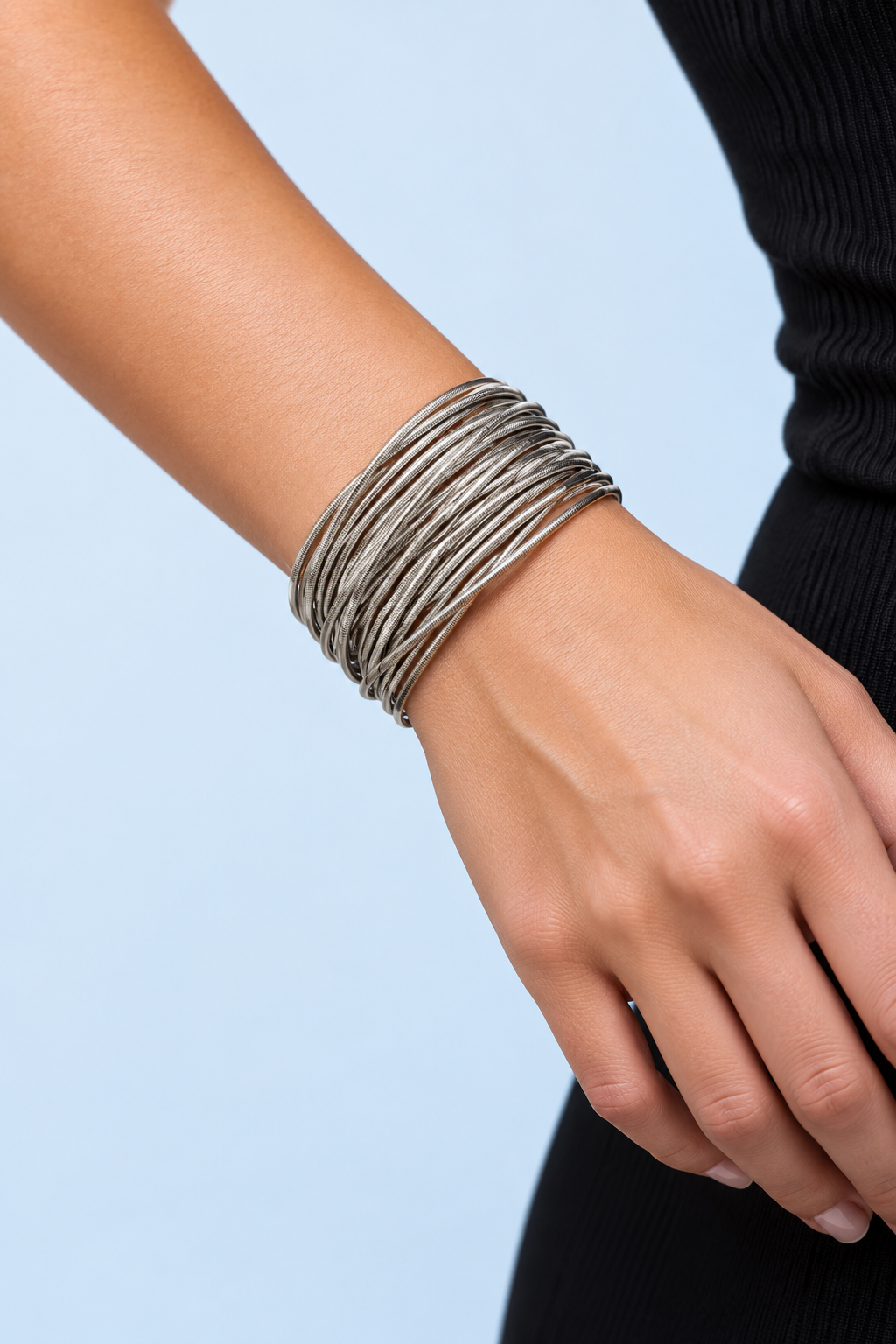 Zadie silver spring bracelets arranged in a circular stack on a pale blue background